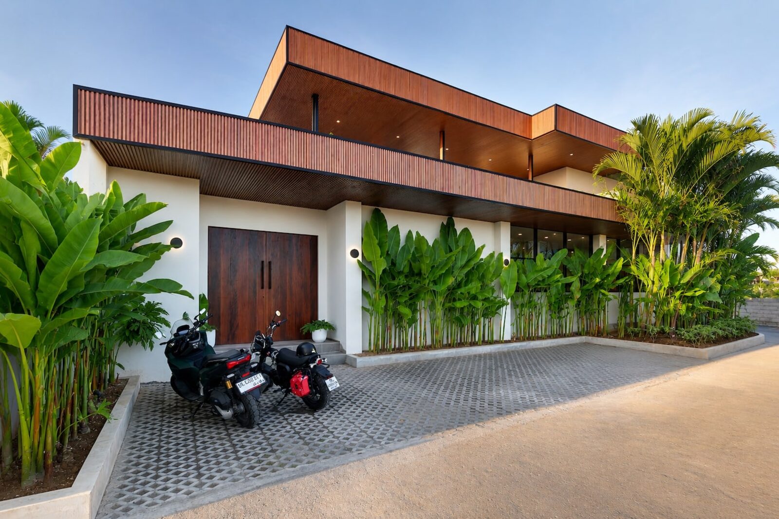 Villa entrance with timber gates, scooters parked in the driveway and banana plants along the wall
