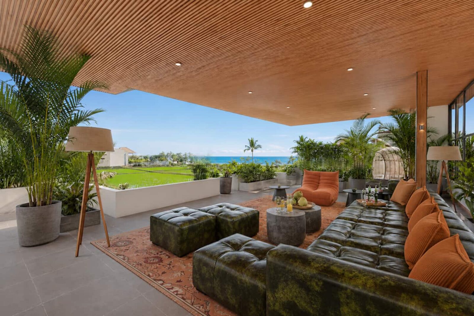 Rooftop lounge under a timber ceiling, deep sofas facing rice fields and the ocean