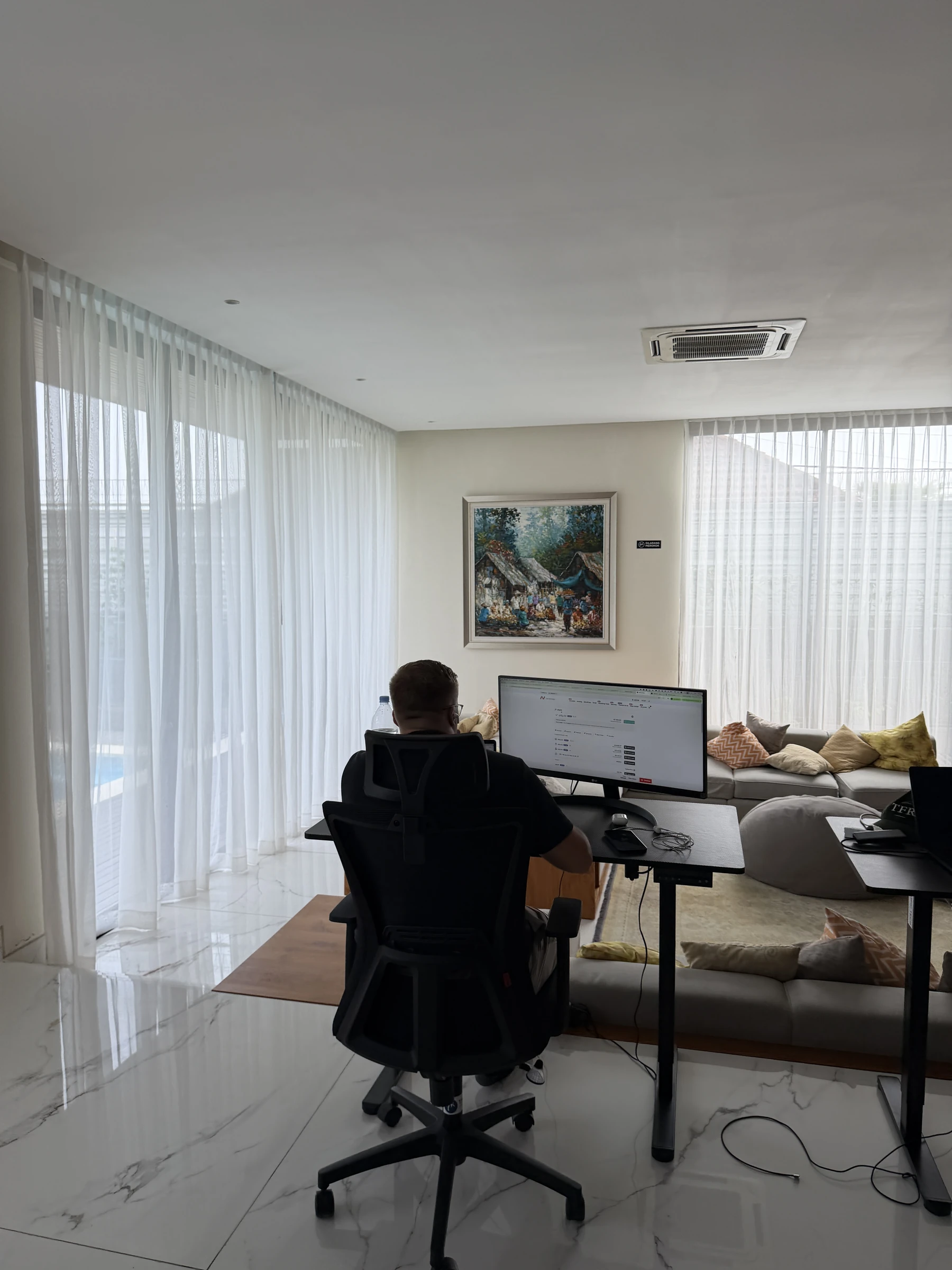 Konzentriertes Arbeiten am Bildschirm, von hinten aufgenommen vor den Vorhängen der Residence auf Bali