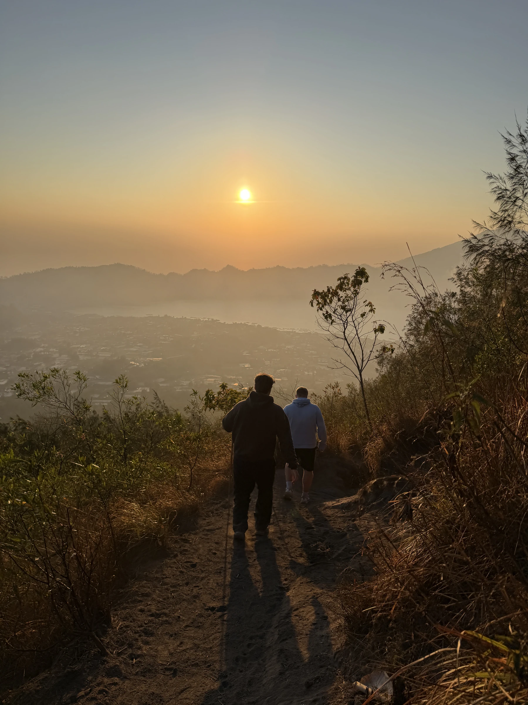 Zwei Teilnehmer gehen im warmen Gegenlicht gemeinsam einen Bergpfad auf Bali entlang